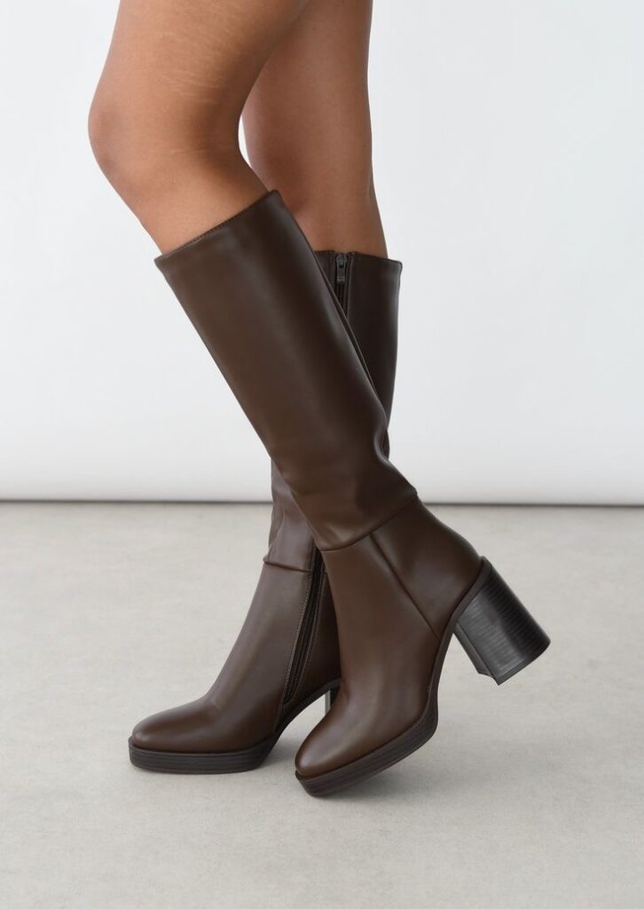 Une paire de bottes en cuir marron à talons, hauteur genoux, alliant élégance et confort. Une pièce intemporelle pour structurer un look automne-hiver.